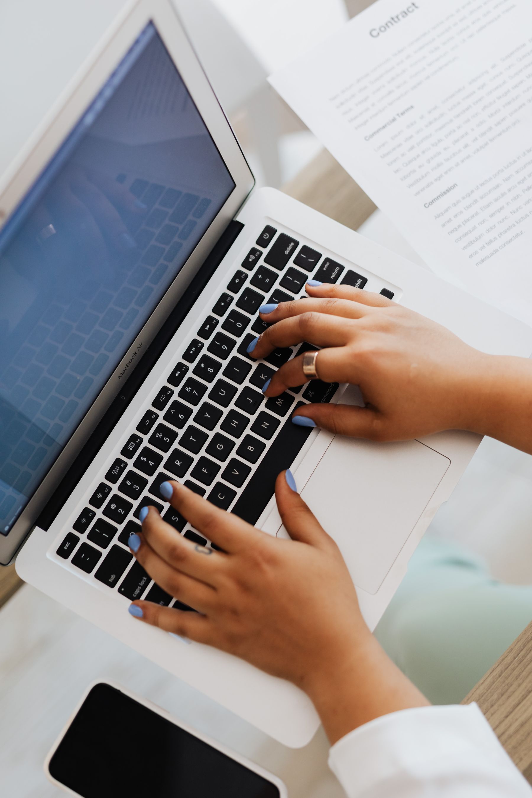 Hands typing on a laptop beside a document