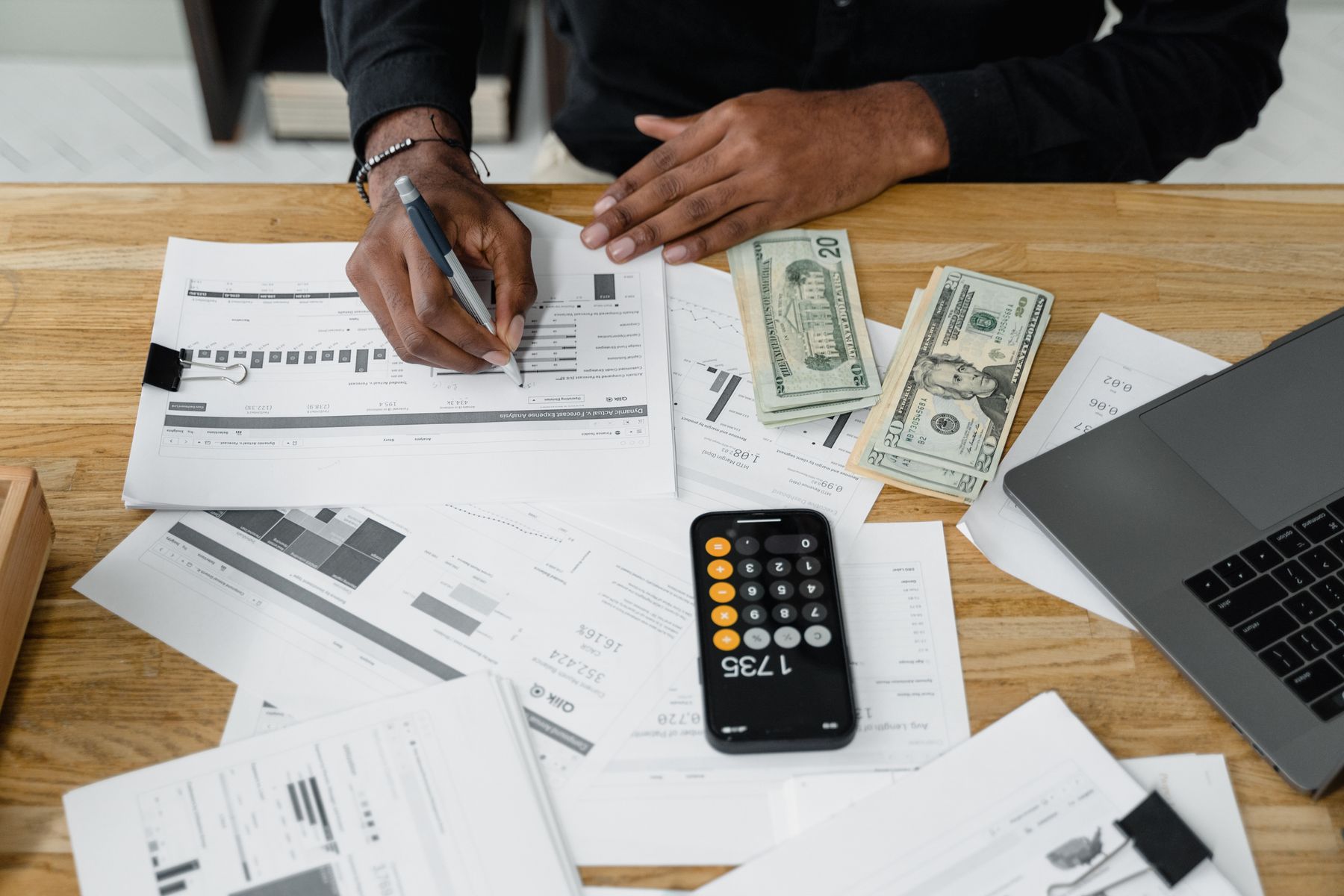 Financial reports, calculator, laptop, and cash arranged on a work desk